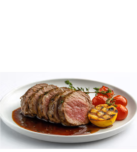A plate of sliced beef tenderloin served with grilled lemon, cherry tomatoes, and a rich demi-glace sauce.